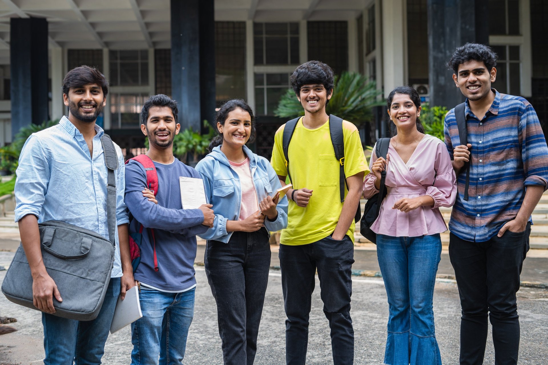 Group of happy students standing with books and backpack at university campus - concept of friendship, togetherness and education