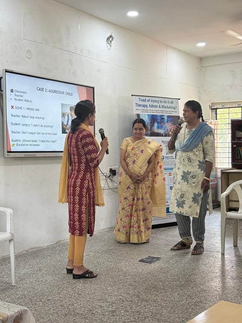 Three women in traditional Indian attire discussing a case study presentation in a clinical classroom setting with a projection screen visible