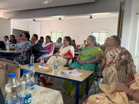 Group of women seated in rows at a community gathering in a bright indoor space with white walls and windows