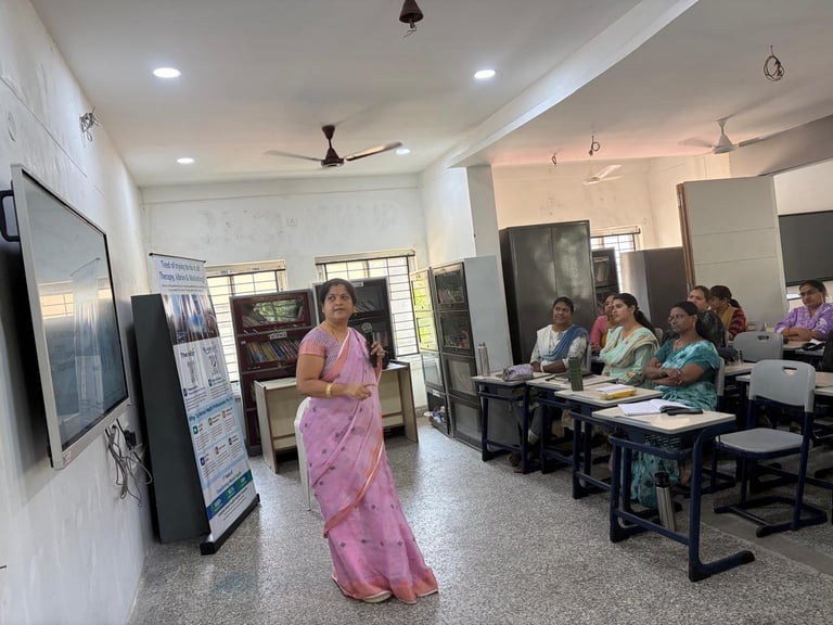 A woman in a pink saree presents to a classroom of seated students in a bright, modern educational facility